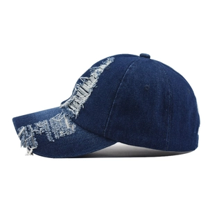 Detailed view of the distressed denim texture and frayed holes on a navy baseball cap