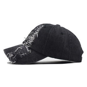 Detail of distressed ripped holes and fringe texture on washed black denim baseball cap