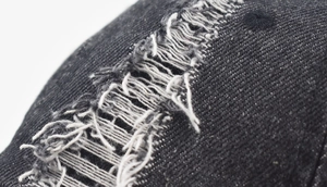 Close-up of distressed black denim baseball cap with vintage frayed hole details