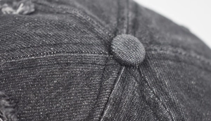 Close-up of the reinforced stitching and top button on a distressed washed denim baseball cap