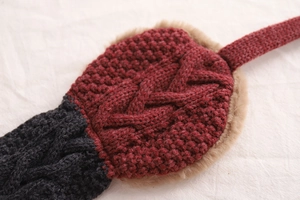 Detailed macro view of dark red cable knit ear muffs with soft beige faux fur lining