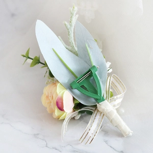 Detail of light orange artificial rose boutonniere with green leaves and gold-edged ribbon