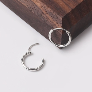 Minimalist silver circular hoop earrings for men and women on a walnut wood block
