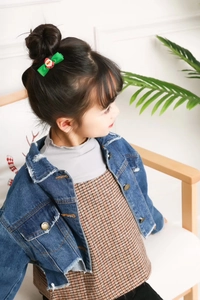 Detail of child wearing a green Santa Claus bow hair clip with a denim jacket