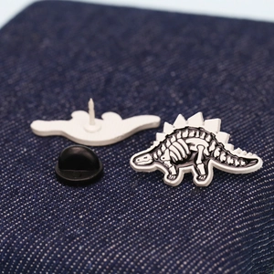 Macro detail of dinosaur skeleton enamel pin with secure black rubber back on denim fabric