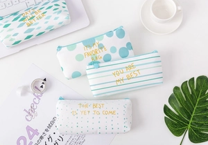 Detailed top view of four canvas pencil cases with gold foil lettering on a desk