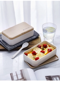 Detail of double-layer lunch box with wooden style lid and spoon on marble surface