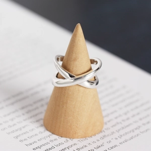 Detail of minimalist S925 silver crossover X ring displayed on a wooden cone stand
