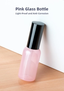 Detailed view of pink translucent glass spray bottle with black cap on wooden surface