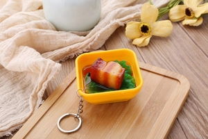 Macro detail of realistic braised pork food model keychain with green vegetables in a bowl