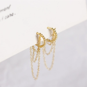 Detail of gold layered chain tassel earrings with granular texture on a white card