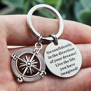 Silver metal keychain with compass charm and engraved dream quote held in hand