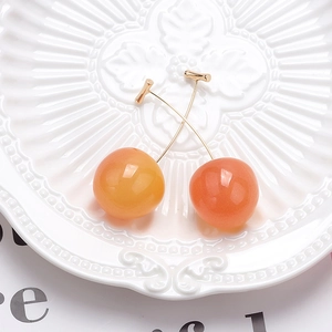 Detail shot of cherry-shaped earrings with orange-red gradient and golden metal stems