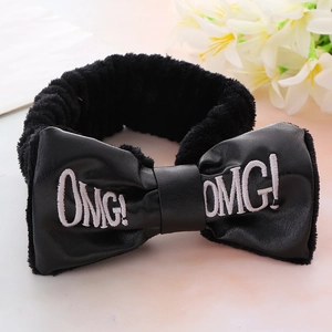Detail shot of black plush headband featuring faux leather OMG bow on pink background