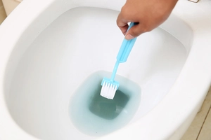 Detail showing a light blue V-shaped toilet brush cleaning the inner rim of a white toilet bowl
