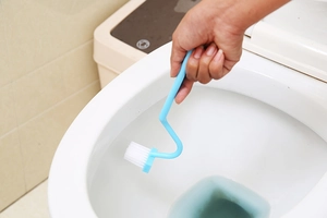 Detail of light blue V-shaped toilet brush cleaning the inner rim of a white toilet bowl