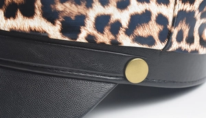 Detailed close-up of leopard print fabric and black leather brim with a gold button