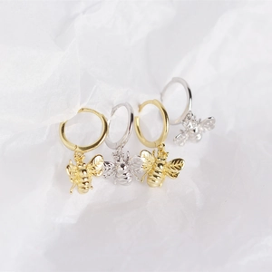 Macro shot of silver and gold bee pendants on round hoops over white textured background