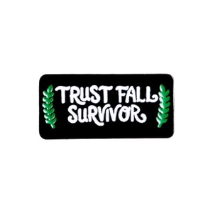 Dettaglio di una spilla in smalto nero con scritta Trust Fall Survivor e foglie