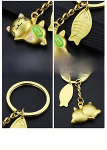 Detail view of gold Maneki Neko keychain featuring fishbone charm and engraved symbols