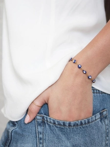 Detail of a gold-tone evil eye bracelet with blue resin charms worn on a female wrist