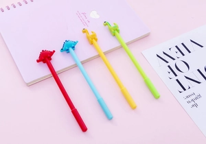 Close-up of four colorful silicone dinosaur pens on a pink desk with notebook