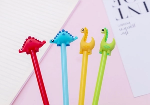 Close-up of four colorful 0.5mm dinosaur gel pens with 3D soft rubber toppers on pink background