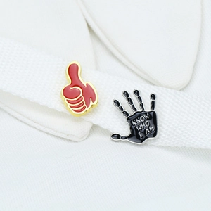 Detailed close-up of colorful enamel hand pins on white fabric, thumb up and palm design