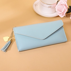 Detail of light blue envelope wallet with gold heart pendant and tassel on beige background