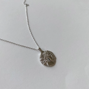 Detail of silver coin necklace featuring a vintage embossed portrait on white background