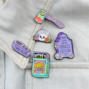 Detail showing five pastel enamel pins including skull and coffin on denim jacket collar