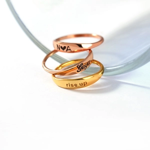Close-up of stacked gold and rose gold hollow rings with personalized engravings on white background