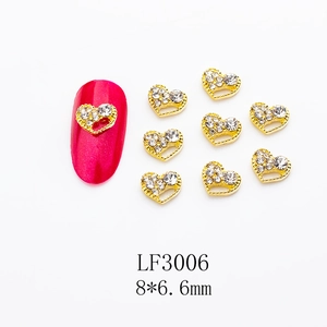 Close-up of heart-shaped alloy nail charms with gold borders and clear rhinestones
