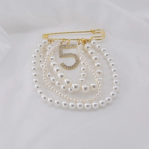Detail of elegant gold brooch featuring layered pearls and rhinestone number 5 on silk