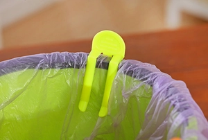 Detail of candy-colored plastic clip securing a trash bag to the rim of a waste bin