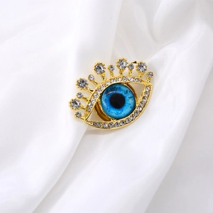 Creative eye-shaped gold brooch with blue iris and sparkling rhinestones on white silk