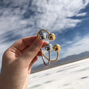 Close-up of minimalist open cuff bracelet with gold and silver polished metal spheres