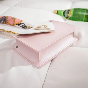 Pink and white contrast shoulder bag for women with gold heart buckle on soft white bedding