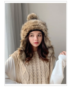 Detail of winter faux fur earflap hat in tan blend with stylish pom-pom accents