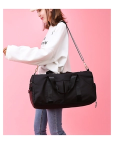 Black gym bag with shoe compartment and adjustable strap on pink background