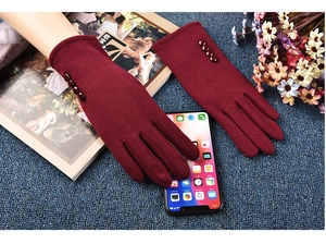 Detail of burgundy touch-screen gloves with four decorative buttons on blue fabric