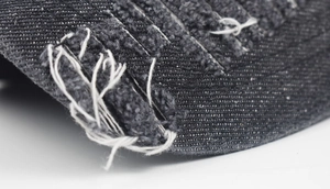 Macro detail of distressed grey denim baseball cap showing torn edges and texture