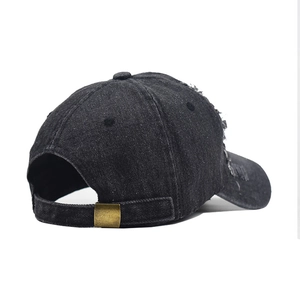 Detail view of washed black denim baseball cap showing distressed holes and metal buckle