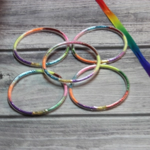 Macro detail of five colorful glitter-filled jelly bangles with rainbow ribbon on wood
