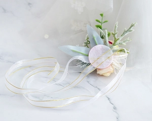 Detailed view of wedding wrist corsage with cream roses and gold-edged organza ribbon