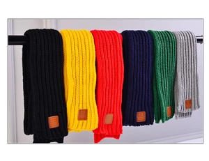 Detail view of colorful knitted scarves with EST MOVE leather patch on a hanging bar