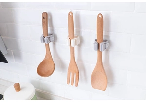 Self-adhesive mop hooks installed on white tiles holding wooden kitchen utensils
