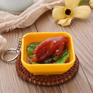 Realistic braised chicken feet miniature food keychain in a yellow bowl on wood background