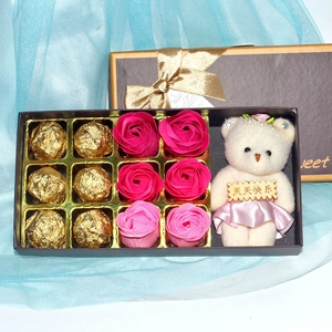 Gift set detail with soap roses, gold-wrapped chocolates, and a plush bear in a pink dress