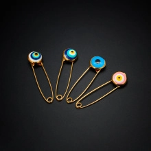 Detailed view of four golden safety pins with multi-colored evil eye beads on black surface